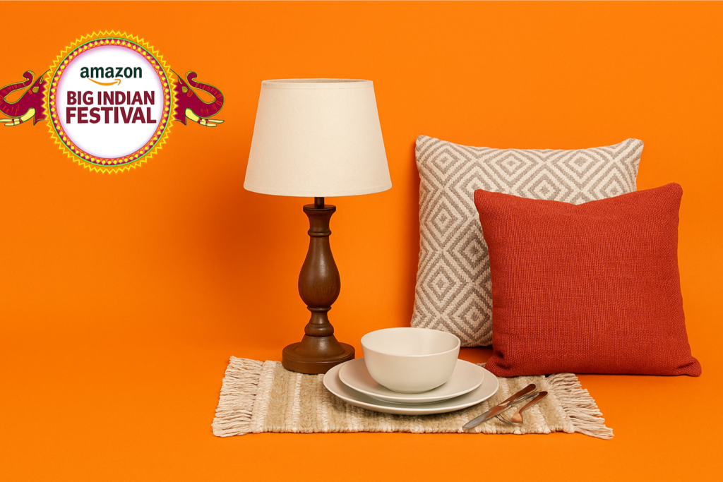 Amazon Big Indian Festival 2025 banner with bedroom side lamp, dinnerware set, cutlery, decorative cushions, and rug on an orange background.